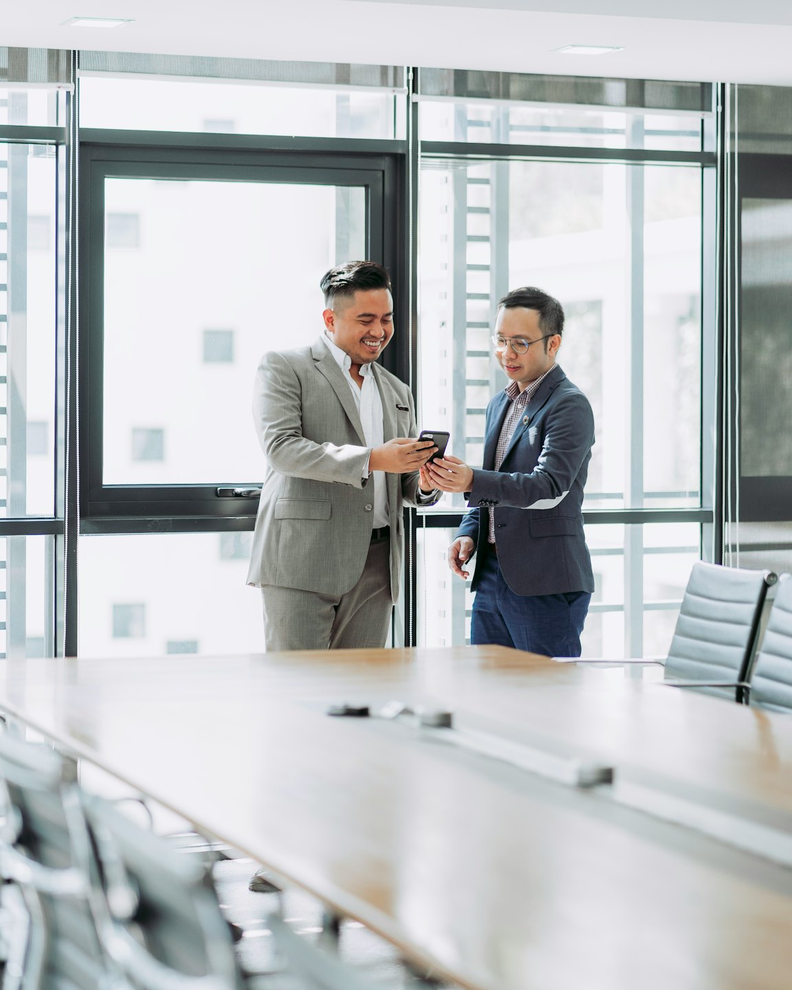 Two men smile while looking at a smartphone in an office.