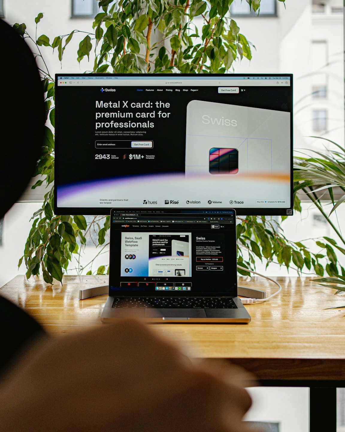 Designer works on a laptop and monitor with website design.